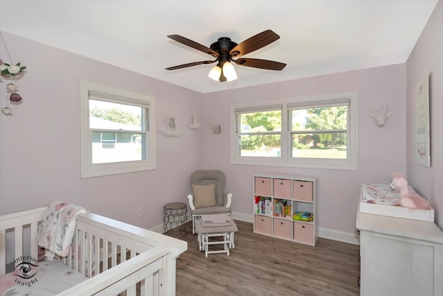 bedroom with a crib, dark hardwood / wood-style floors, multiple windows, and ceiling fan