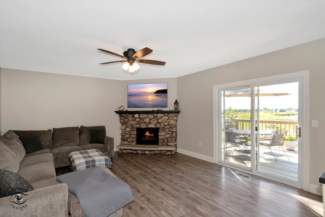 living room featuring ceiling fan, hardwood / wood-style floors, and a stone fireplace