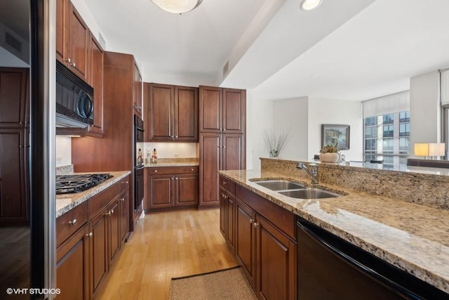 kitchen featuring black appliances, light wood-type flooring, light stone countertops, and sink