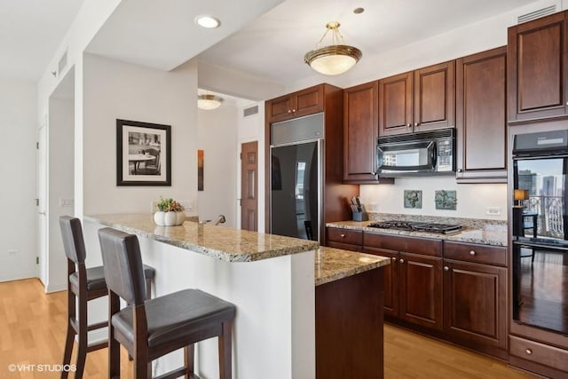 kitchen featuring light stone counters, kitchen peninsula, a kitchen bar, black appliances, and light wood-type flooring