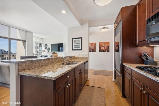 kitchen with dark brown cabinetry, sink, light stone counters, appliances with stainless steel finishes, and light wood-type flooring