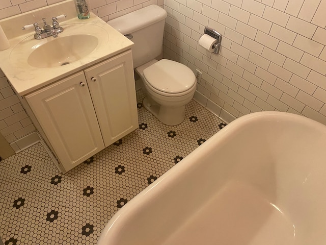 bathroom with vanity, toilet, tile walls, and a washtub