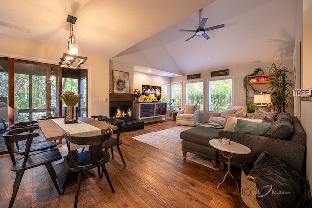 dining room with wood-type flooring, ceiling fan with notable chandelier, high vaulted ceiling, and a large fireplace