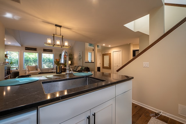 kitchen featuring pendant lighting, dark stone counters, dark wood-type flooring, sink, and white cabinetry