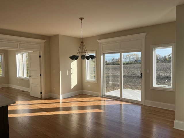 unfurnished dining area with a wealth of natural light, an inviting chandelier, and hardwood / wood-style flooring