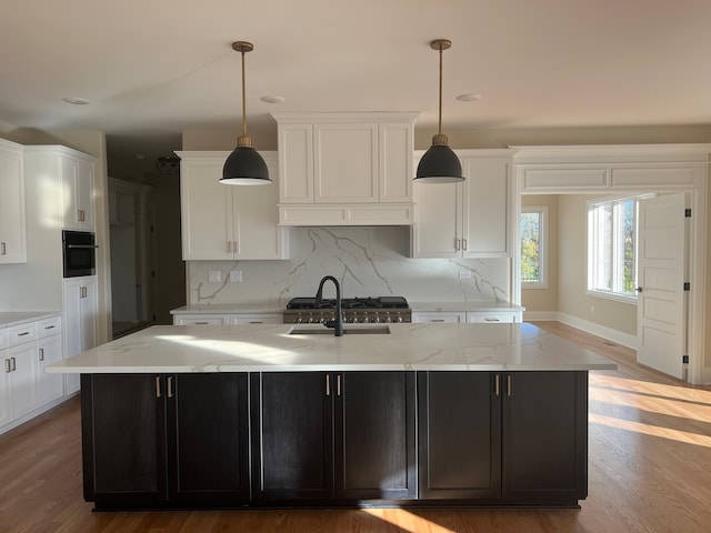 kitchen with hanging light fixtures, hardwood / wood-style flooring, tasteful backsplash, a kitchen island with sink, and black oven