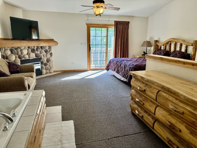 carpeted bedroom featuring access to outside, a stone fireplace, and ceiling fan