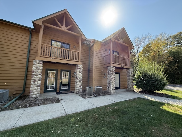 view of front of property featuring french doors, cooling unit, a balcony, and a front lawn