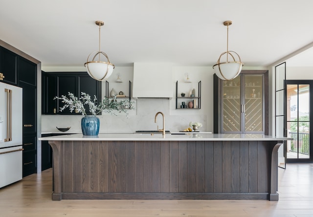 kitchen with a kitchen island, white fridge with ice dispenser, sink, pendant lighting, and light hardwood / wood-style flooring