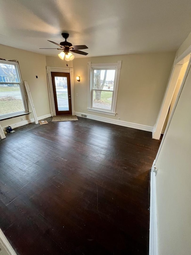 empty room with ceiling fan, dark wood-type flooring, and a wealth of natural light