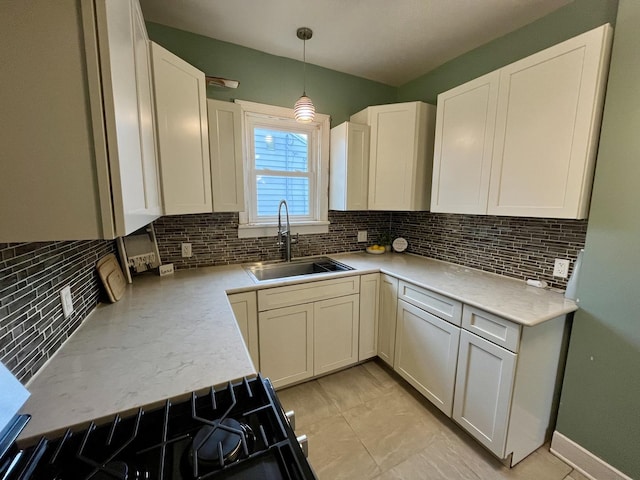 kitchen with stove, sink, tasteful backsplash, decorative light fixtures, and white cabinetry