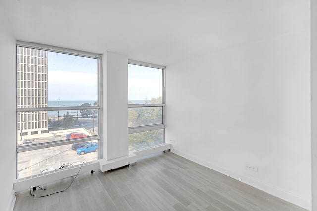 empty room with a wall of windows, light hardwood / wood-style flooring, a water view, and a healthy amount of sunlight