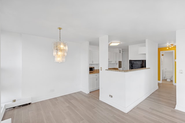 kitchen with light hardwood / wood-style floors, black fridge, pendant lighting, a notable chandelier, and white cabinetry