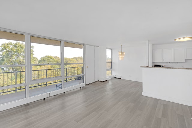 unfurnished living room featuring an inviting chandelier, light wood-type flooring, and a healthy amount of sunlight