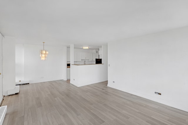 unfurnished living room featuring a chandelier and light hardwood / wood-style flooring