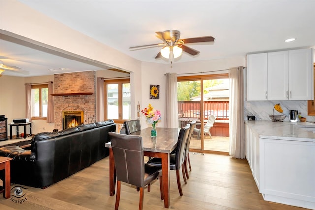 dining area featuring light hardwood / wood-style flooring, a brick fireplace, and ceiling fan