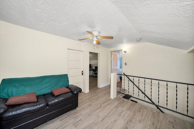 living room featuring light hardwood / wood-style floors, ceiling fan, a textured ceiling, and vaulted ceiling