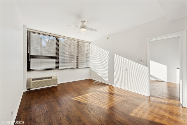 spare room featuring a wall unit AC, ceiling fan, and dark wood-type flooring