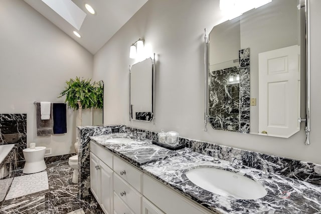 bathroom with vanity, vaulted ceiling with skylight, a washtub, and toilet