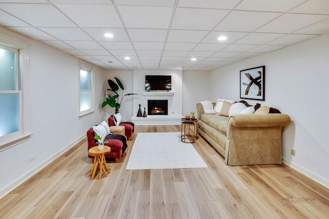 living room with a drop ceiling, a fireplace, and light wood-type flooring