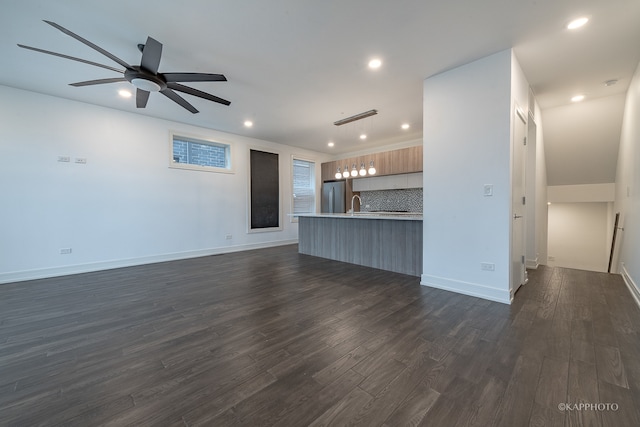 unfurnished living room with ceiling fan, sink, and dark wood-type flooring