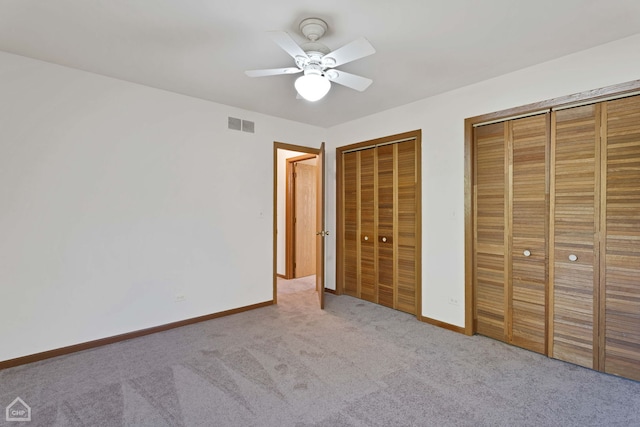 unfurnished bedroom with ceiling fan, light carpet, and two closets