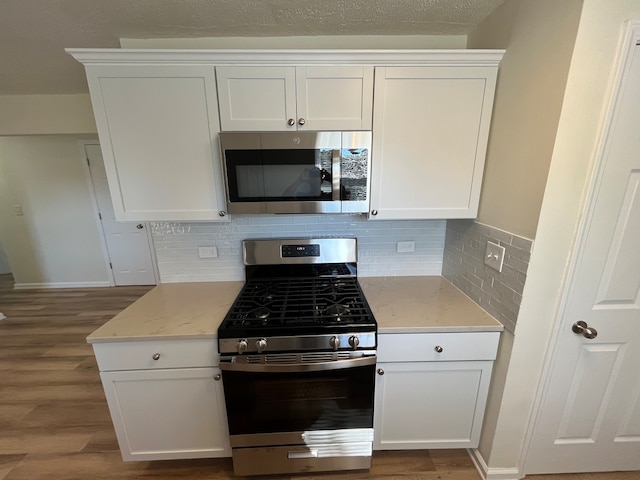 kitchen with hardwood / wood-style flooring, stainless steel appliances, tasteful backsplash, and white cabinets