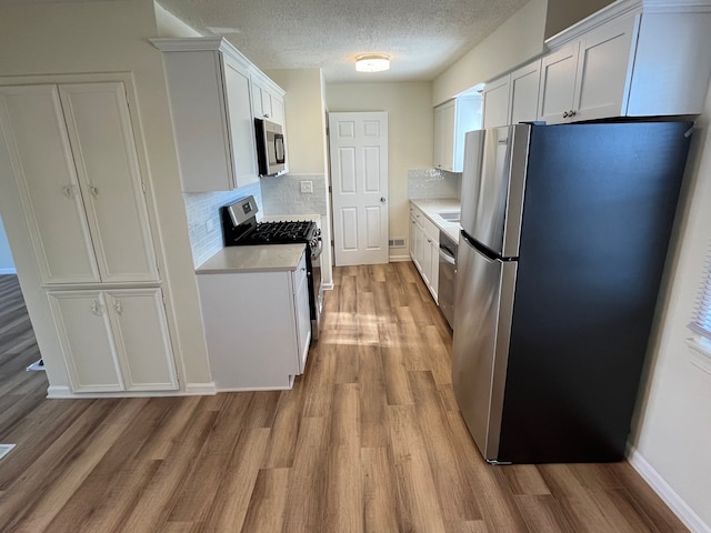 kitchen featuring decorative backsplash, white cabinetry, a textured ceiling, light wood-type flooring, and stainless steel appliances