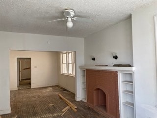 unfurnished living room featuring a brick fireplace, a textured ceiling, and ceiling fan