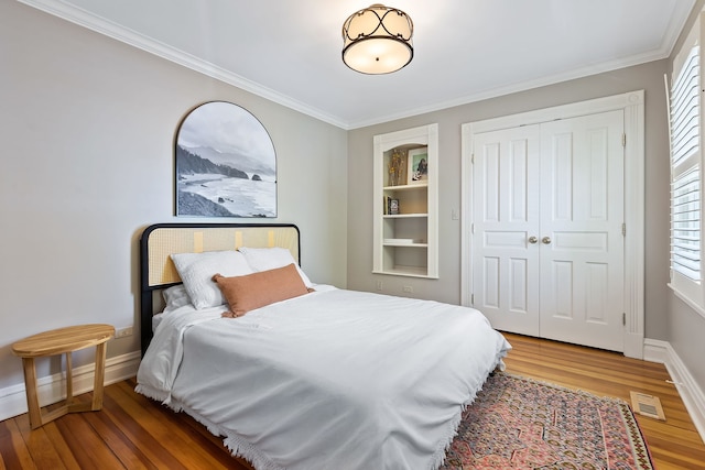 bedroom featuring wood finished floors, visible vents, baseboards, ornamental molding, and a closet