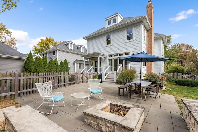 rear view of house with a chimney, a patio area, fence, and a fire pit