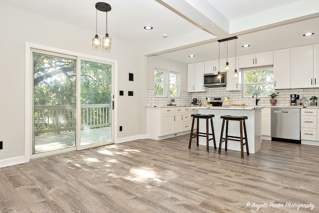 kitchen with appliances with stainless steel finishes, white cabinetry, light wood-type flooring, and pendant lighting