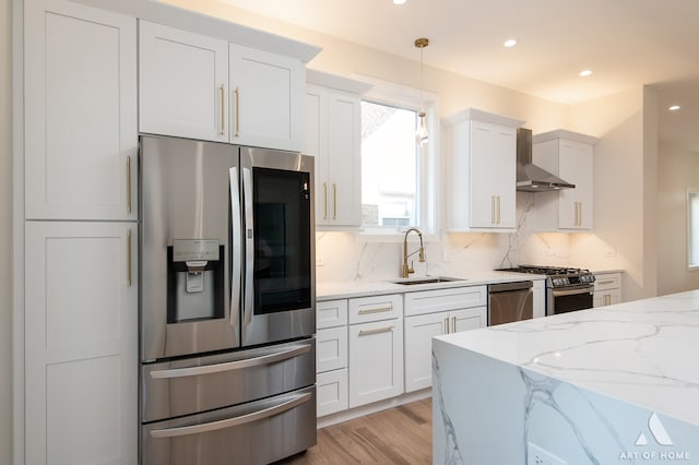 kitchen featuring wall chimney range hood, tasteful backsplash, appliances with stainless steel finishes, white cabinetry, and sink