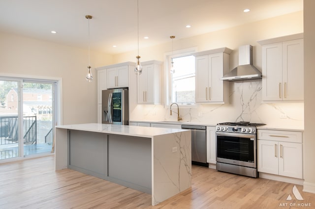 kitchen with wall chimney exhaust hood, appliances with stainless steel finishes, hanging light fixtures, and plenty of natural light