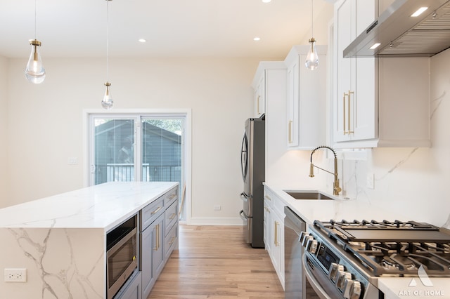 kitchen featuring white cabinetry, stainless steel appliances, wall chimney exhaust hood, decorative light fixtures, and light stone counters