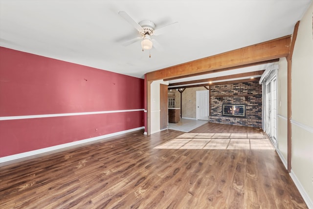 unfurnished living room featuring a brick fireplace, dark hardwood / wood-style floors, beam ceiling, and ceiling fan