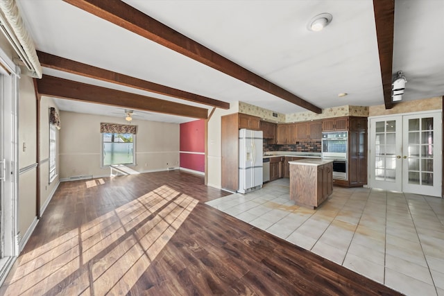 kitchen with tasteful backsplash, white appliances, french doors, a kitchen island, and light hardwood / wood-style floors