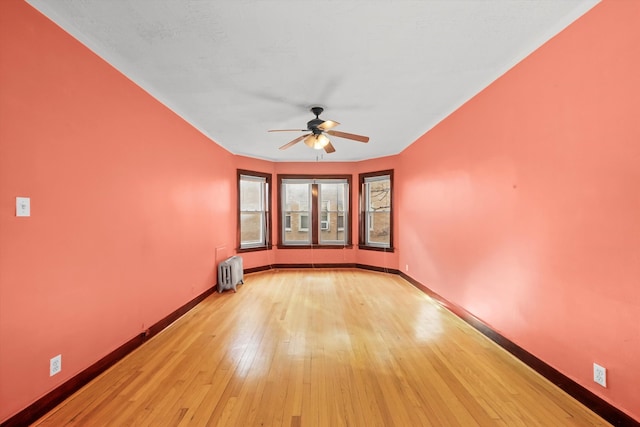 empty room with ceiling fan, light hardwood / wood-style floors, and radiator