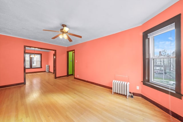 empty room with radiator heating unit, ceiling fan, light wood-type flooring, and a wealth of natural light