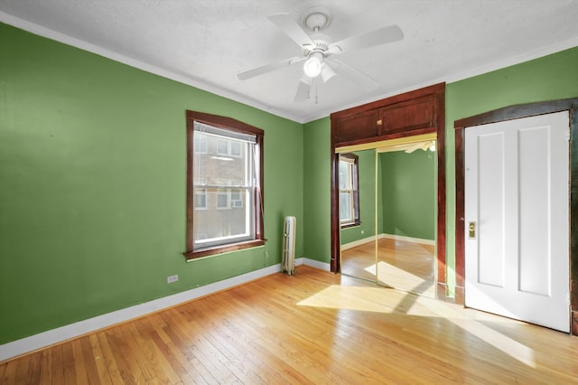 unfurnished bedroom featuring radiator heating unit, a closet, ceiling fan, ornamental molding, and light hardwood / wood-style flooring