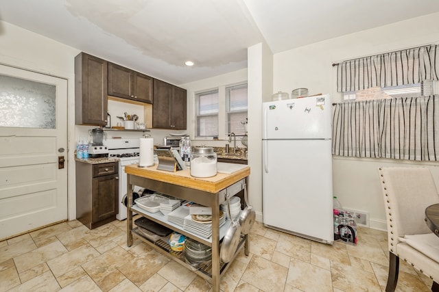 kitchen with dark brown cabinets, light stone counters, and white appliances