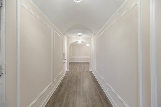 hallway featuring arched walkways, dark wood-style flooring, vaulted ceiling, and a decorative wall