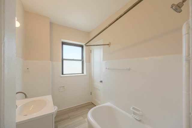 full bath with toilet, vanity, tile walls, wainscoting, and a bathtub