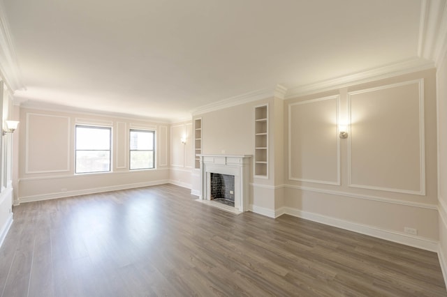 unfurnished living room featuring built in shelves, dark wood-style floors, crown molding, a fireplace with flush hearth, and baseboards