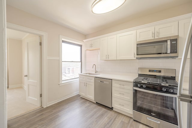 kitchen with white cabinets, decorative backsplash, appliances with stainless steel finishes, light countertops, and a sink