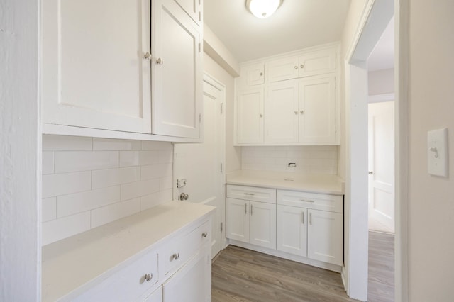 kitchen featuring light countertops, light wood-type flooring, backsplash, and white cabinetry