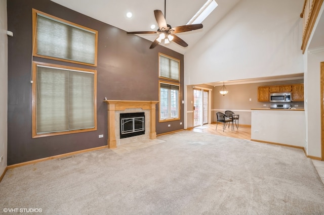 unfurnished living room featuring a tiled fireplace, light carpet, high vaulted ceiling, ceiling fan, and a skylight