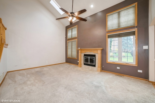 unfurnished living room with light colored carpet, a tile fireplace, high vaulted ceiling, ceiling fan, and a skylight