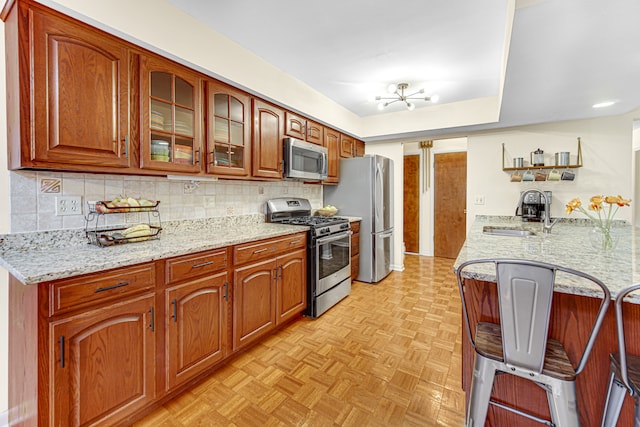 kitchen featuring sink, stainless steel appliances, an inviting chandelier, tasteful backsplash, and light stone counters