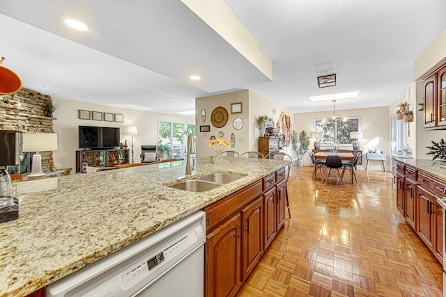 kitchen with light stone counters, white dishwasher, light parquet floors, sink, and a stone fireplace